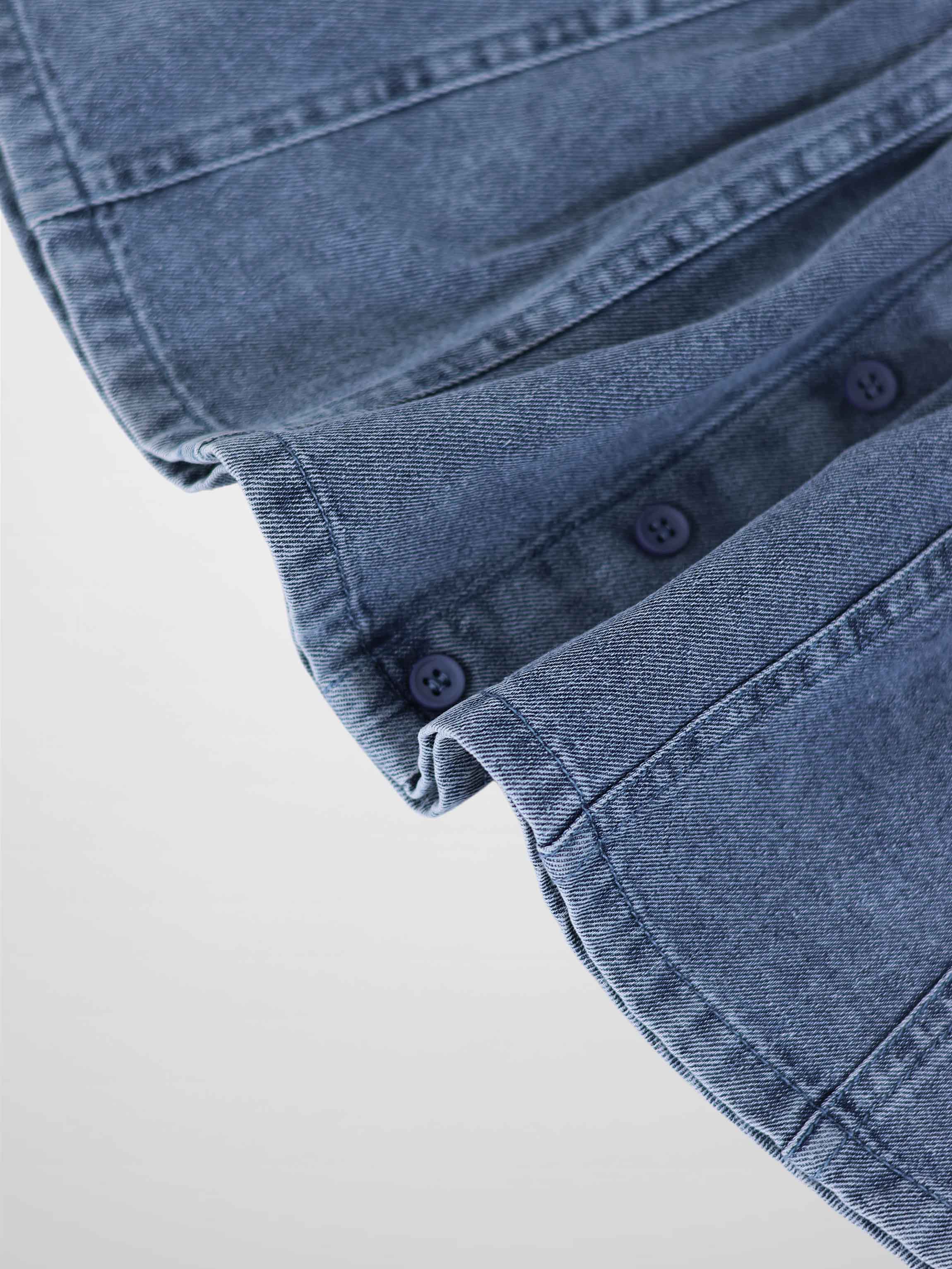 Paneled blue denim fabric close-up with seam lines and blue buttons.
