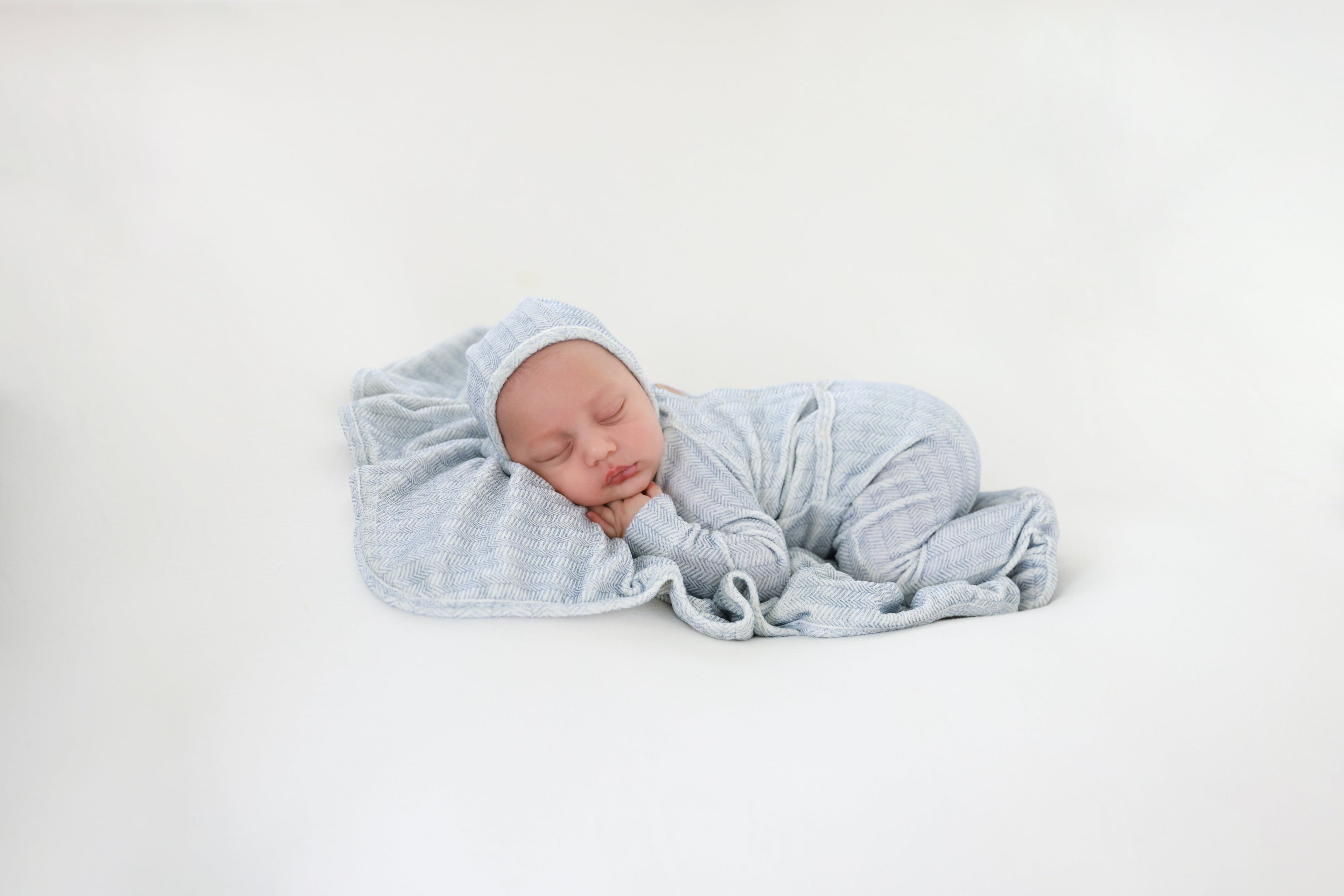 Heritage Herringbone Blue layette set, baby swaddled in blue herringbone fabric.