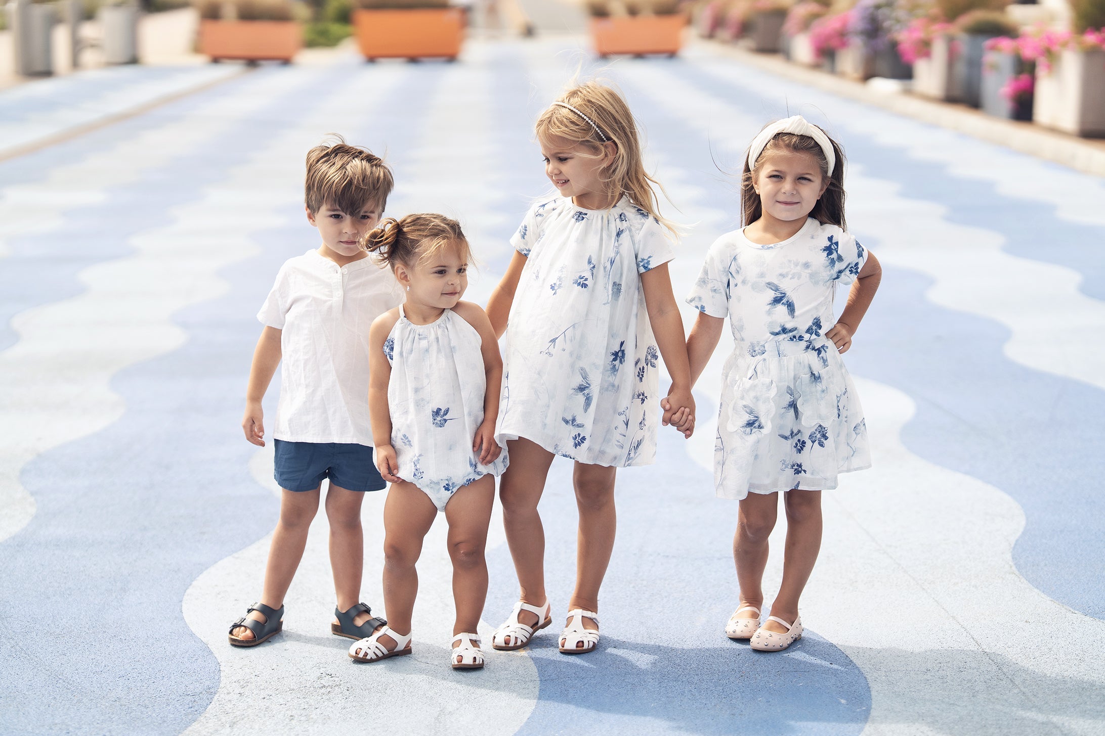 Four children in white and blue floral outfits stand on a wavy blue patterned walkway.