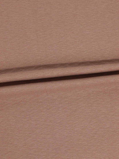 Dusty pink textured stretchy fabric close-up with a fold.