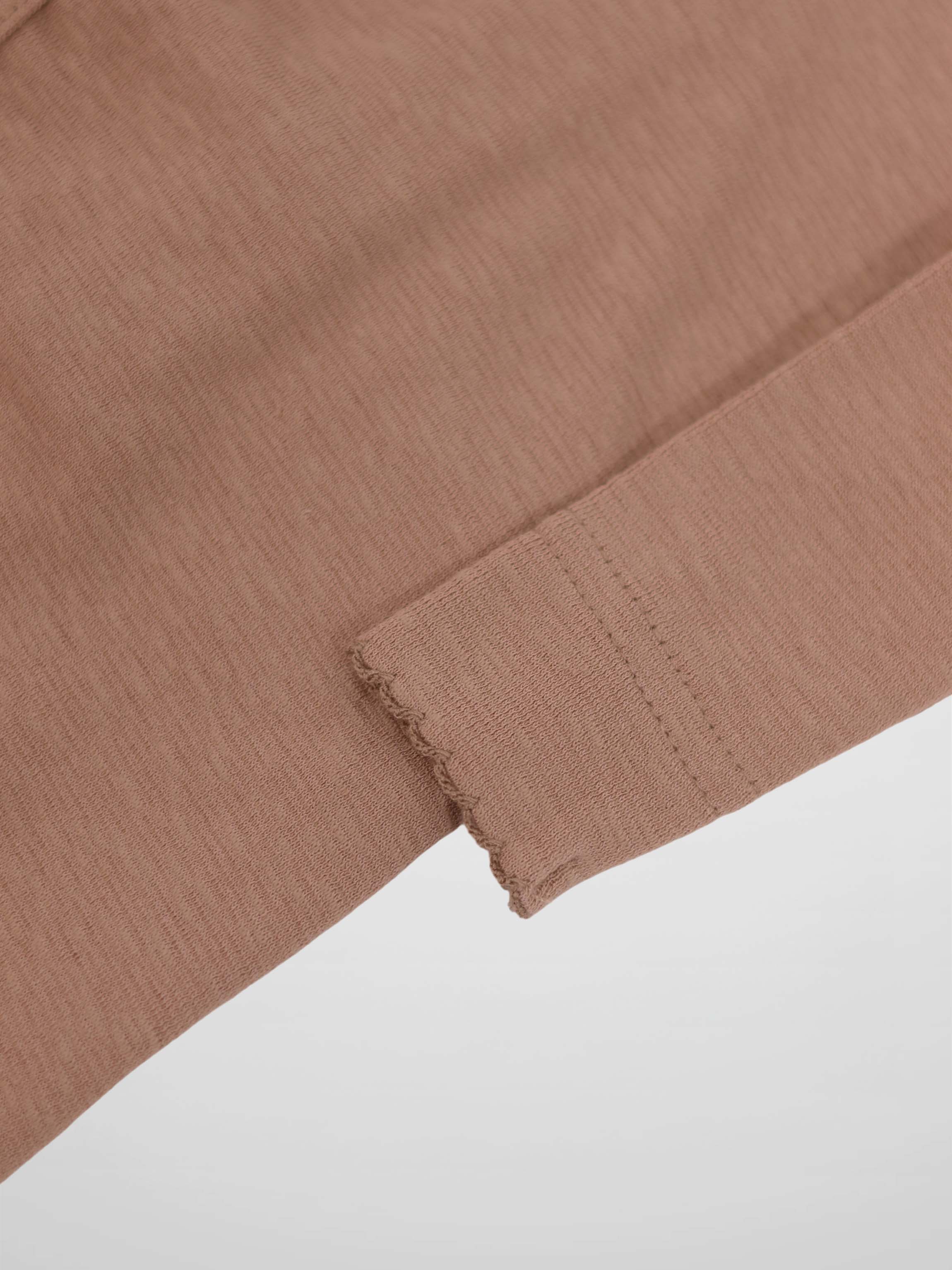 Dusty pink knit sleeve close-up with scalloped edge trim on a soft, stretchy baby jumpsuit.