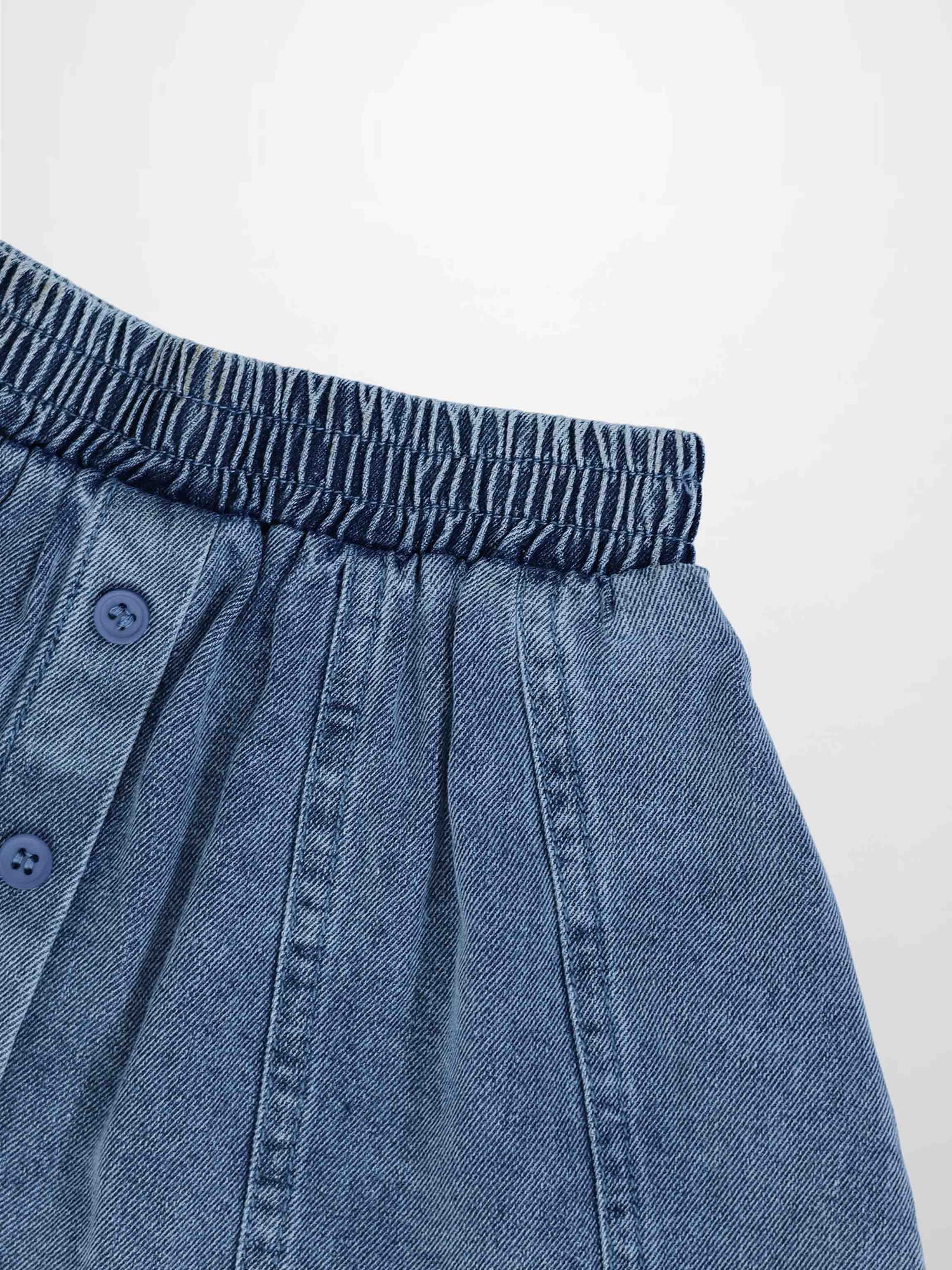 Paneled blue denim skirt with elastic waistband and front button placket.
