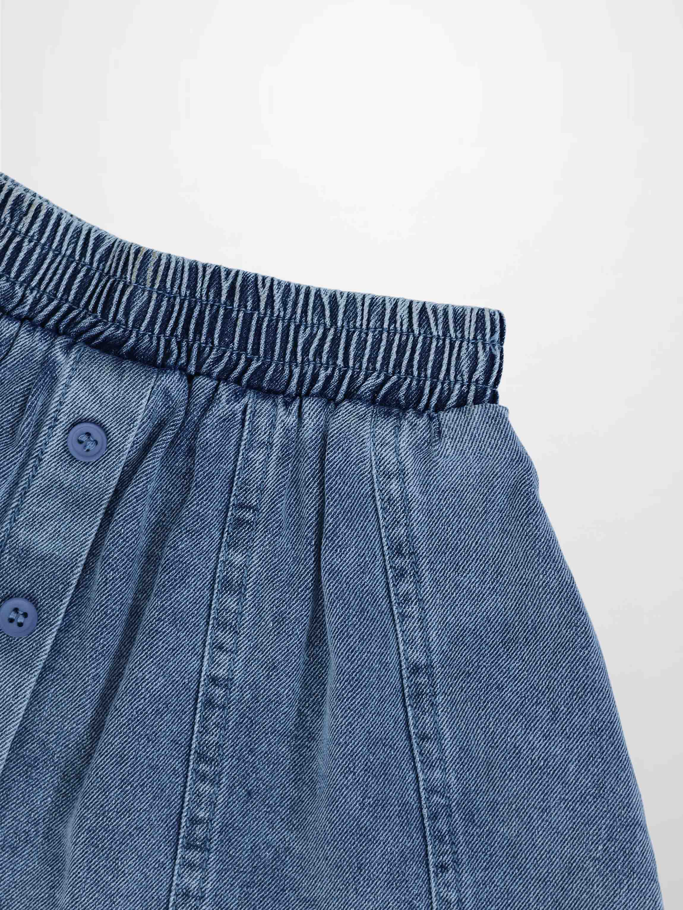 Paneled blue denim skirt with elastic waistband and front button placket.