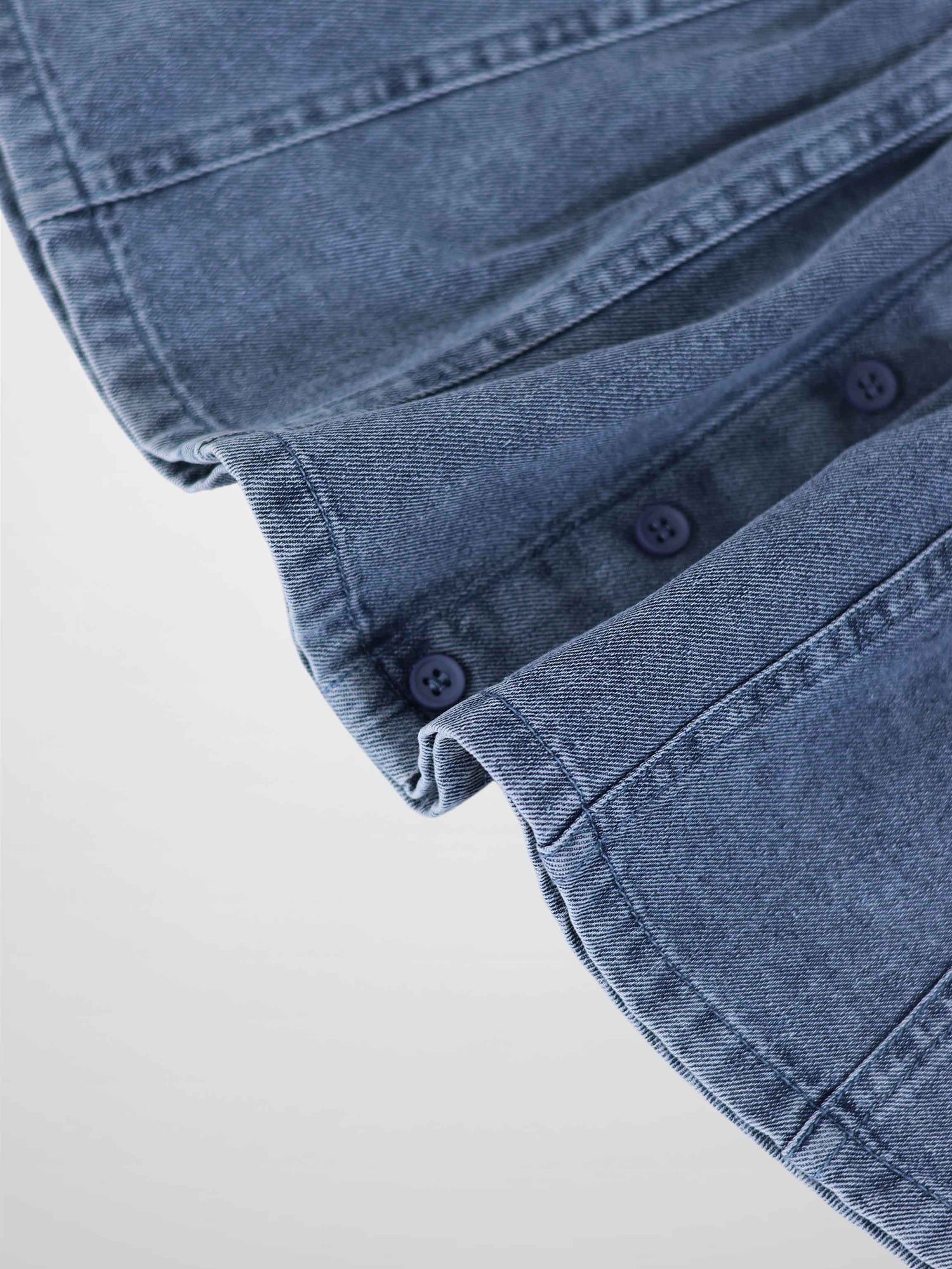 Paneled blue denim fabric close-up with seam lines and blue buttons.