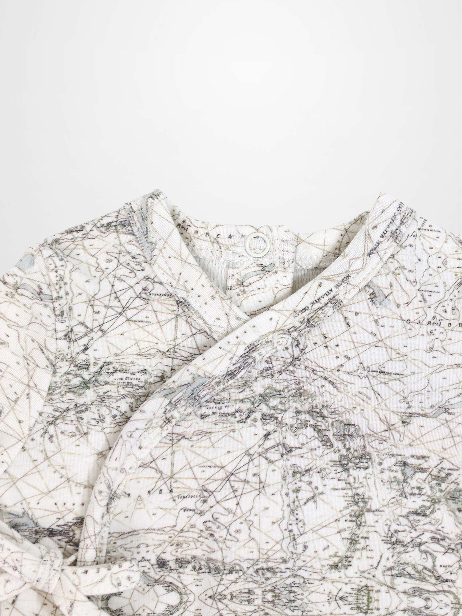 Map Stretchy baby jumpsuit footie with sage-green map lines, compass markers on off-white fabric.