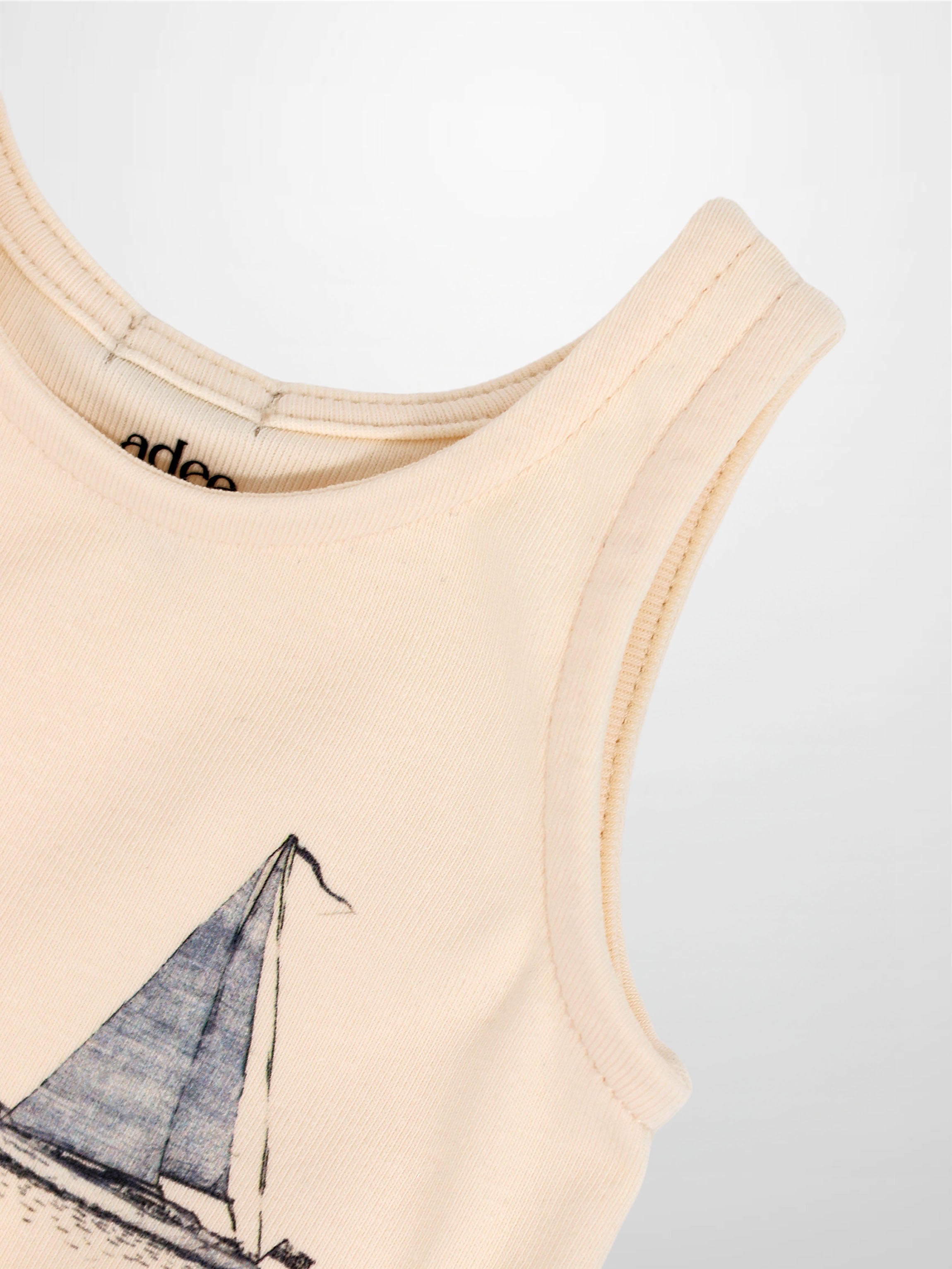 Beige sleeveless romper with sailboat graphic, close-up of neckline.