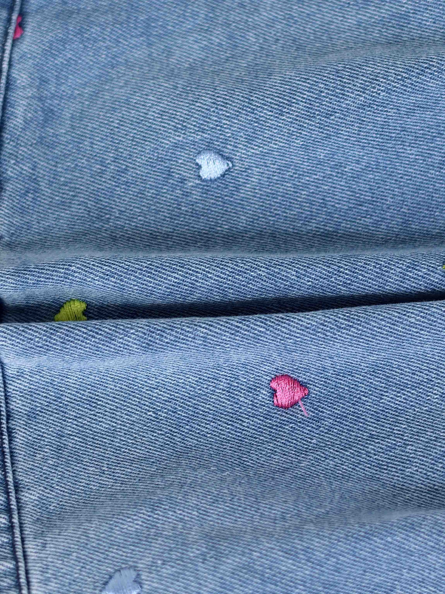Light-wash denim shorts featuring tiny multicolor embroidered heart patches on the pockets.