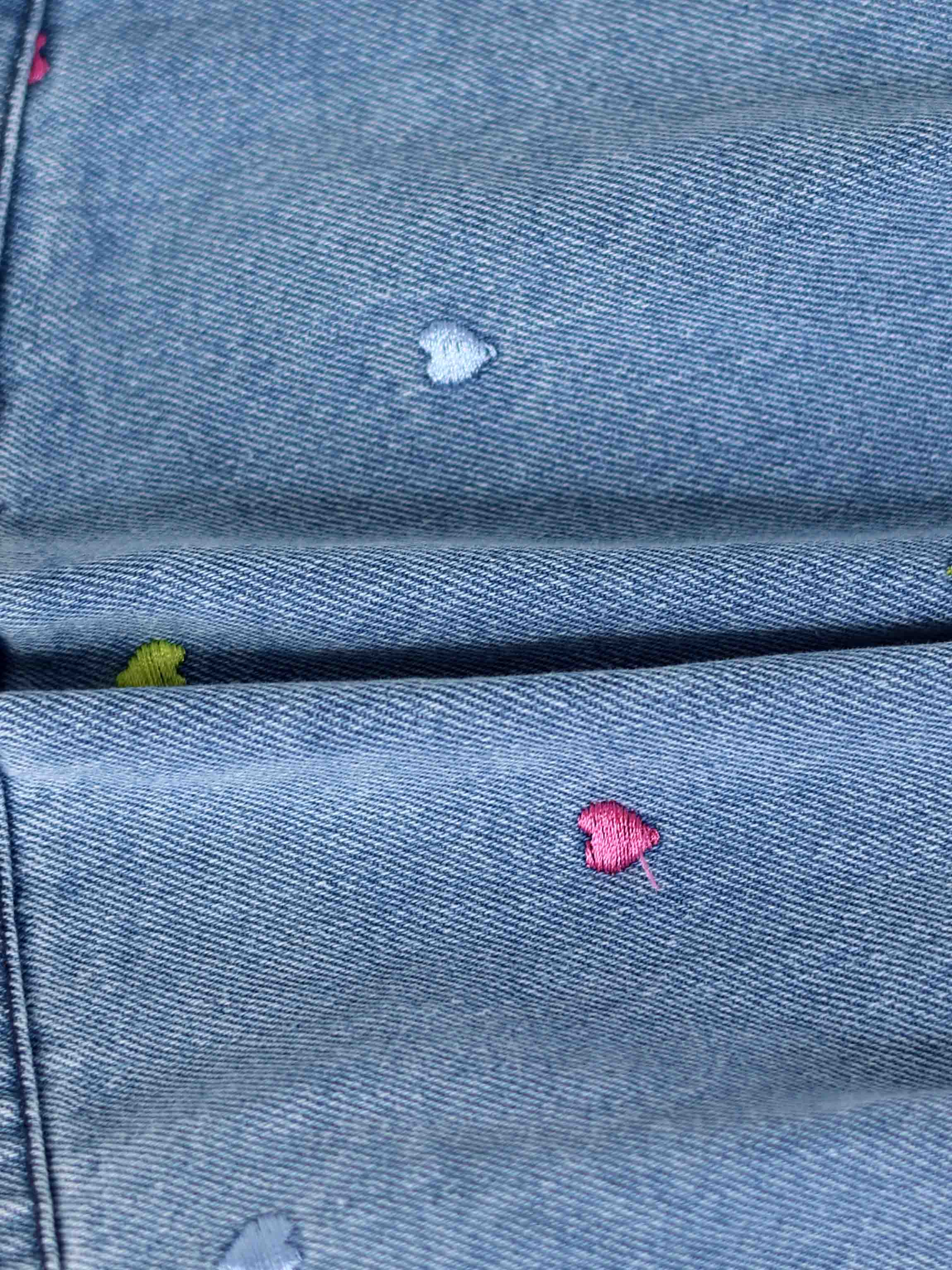 Light-wash denim shorts featuring tiny multicolor embroidered heart patches on the pockets.