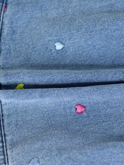 Light-wash denim shorts featuring tiny multicolor embroidered heart patches on the pockets.