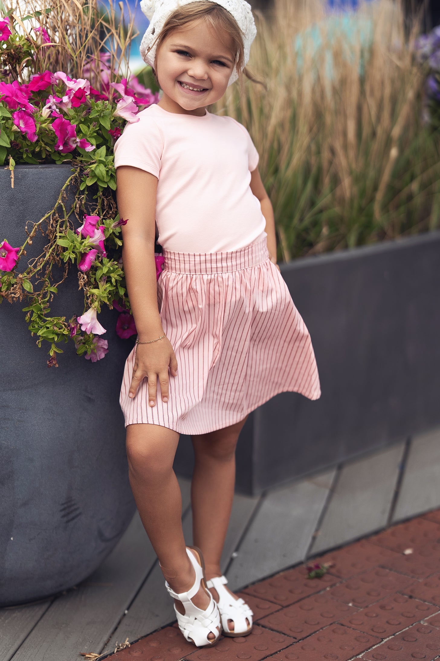 Pink striped cotton skirt worn by a girl in pale pink top outdoors.