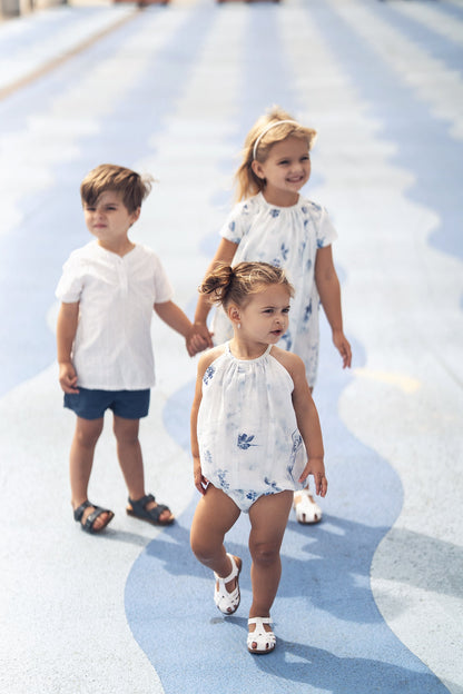 Three children in textured white cotton outfits walking on blue patterned surface.